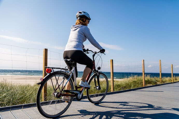 Mulher com capacete andando de bicicleta em avenida perto da praia