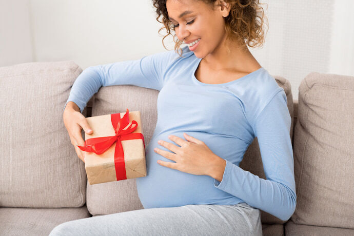 Mulher grávida sorrindo para a barriga enquanto segura presente