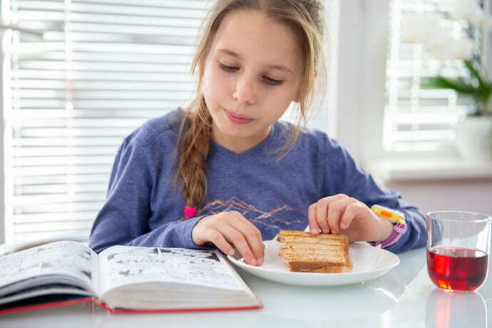 Menina tomando café da manhã e lendo gibi.