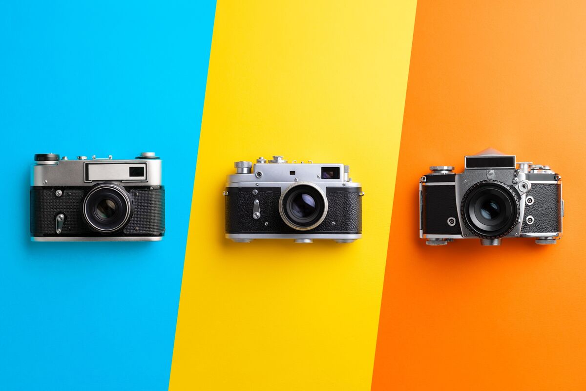 Três câmeras a frente de fundos coloridos (azul, amarelo e laranja), posicionadas lado a lado