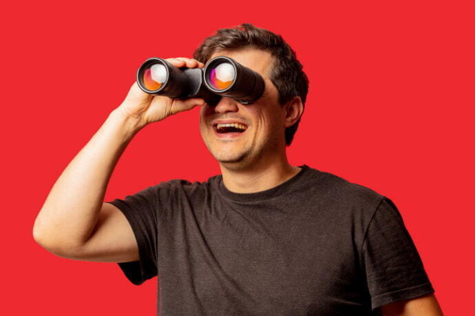 Homem segurando binóculo nos olhos em um fundo vermelho