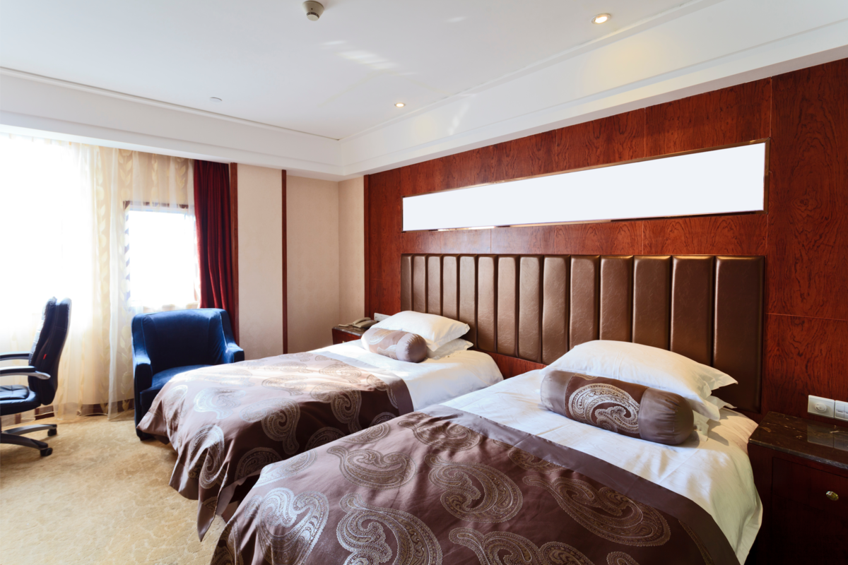Um quarto pequeno de hotel com camas e uma janela que traz claridade