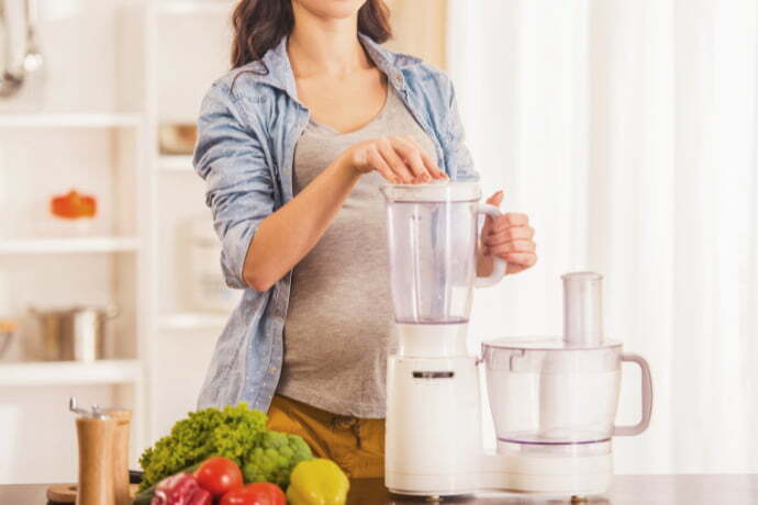 Mulher grávida cozinhando com processador de alimentos.