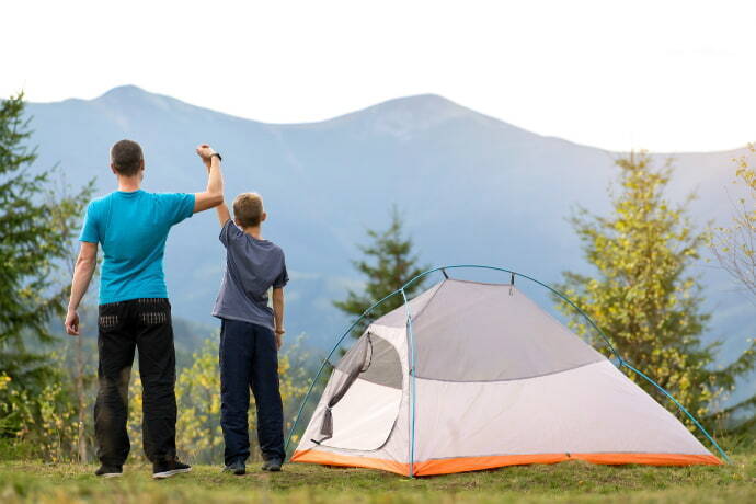 Pai e filho erguendo os braços próximos há uma barraca de camping 