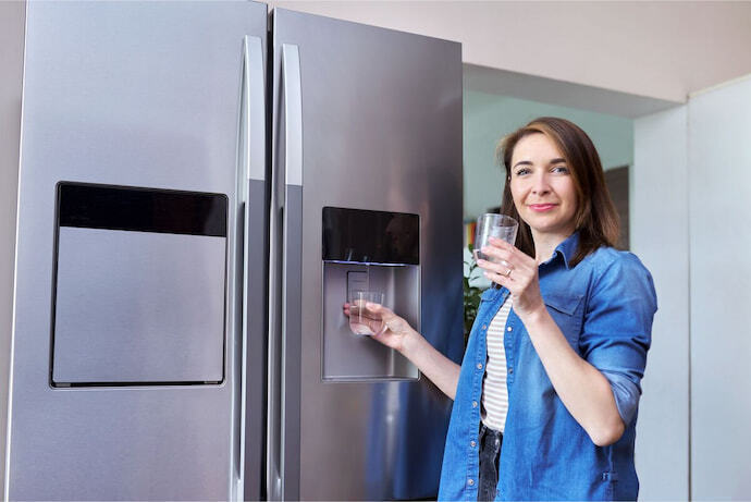 Mulher enchendo copo no dispenser da geladeira 