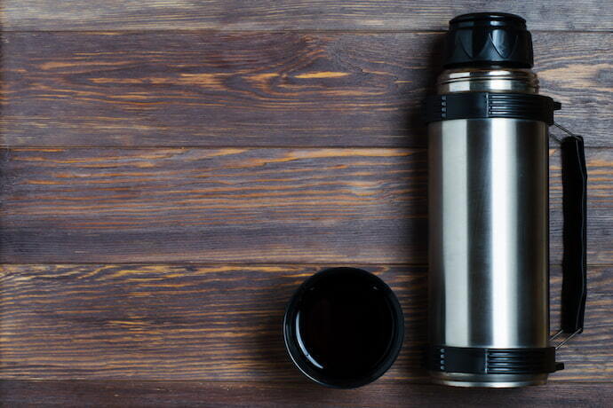 Garrafa térmica, chá quente ou café em uma caneca, na superfície de madeira.