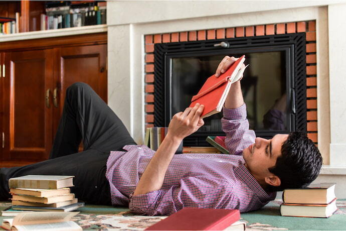 Homem lendo um deitado sobre um tapete cheio de livros em uma elegante sala de estar.