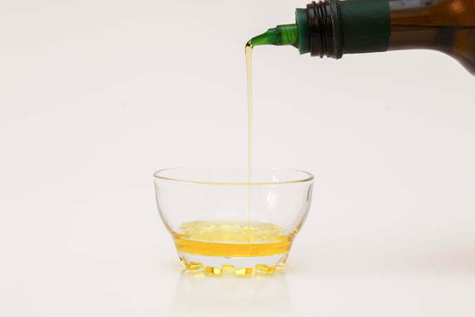 Azeite de oliva sendo derramado em pequeno pote a partir de garrafa com bico dosador
