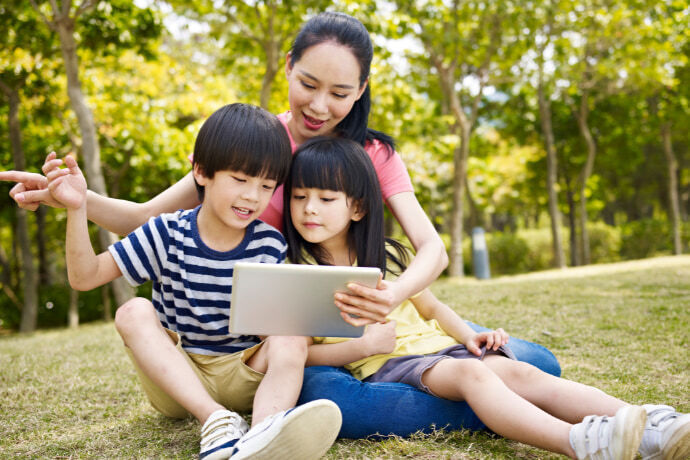 Mãe e dois filhos mexendo no tablet em um parque