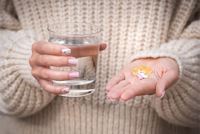 Mãos femininas segurando um copo de água, vitaminas e suplementos.