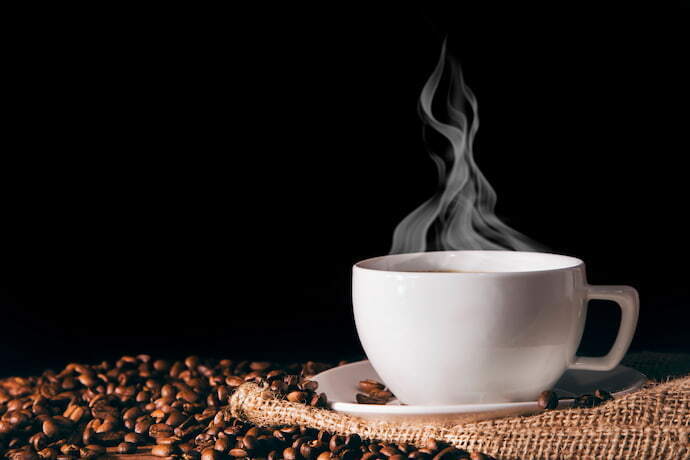 Xícara de café com grãos em volta em fundo preto