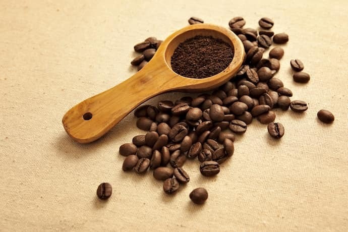 Grãos de café e colher de madeira com café em pó