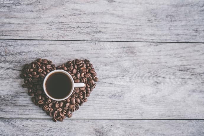Grãos de café formando um coração junto de uma xícara de café