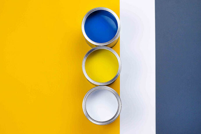 Três latas de tinta em fundo amarelo, azul e branco