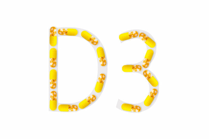 Cápsulas de vitamina amarelas formando "D3" em fundo branco.