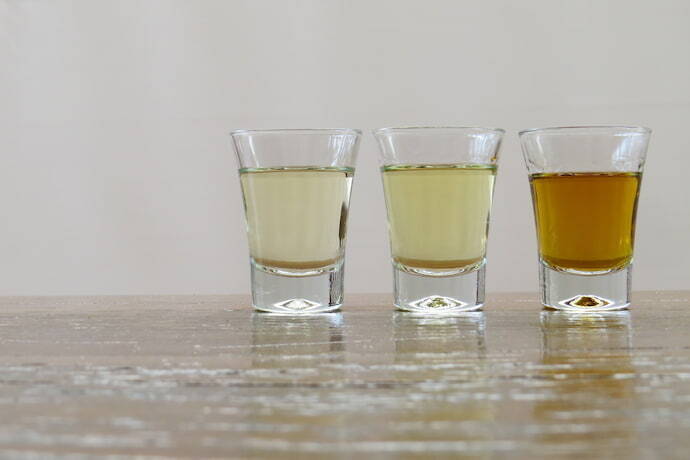 Três copos de shot com cachaça de diferentes tipos e cores