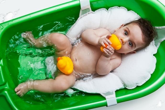 Bebê em banheira verde com almofada para banho branca.
