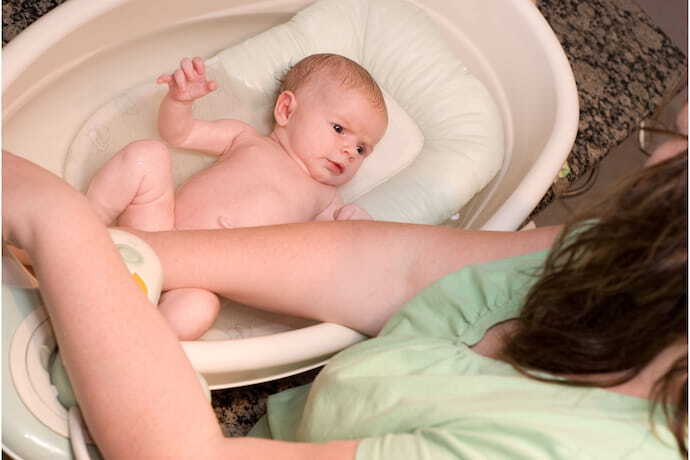 Bebê em banheira rosa claro com almofada para banho branca. 