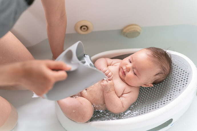 Bebê na banheira com almofada para banho branca e cinza.