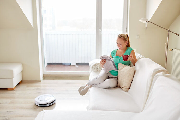 Mulher lendo jornal em sala de estar enquanto um robô aspirador limpa o chão