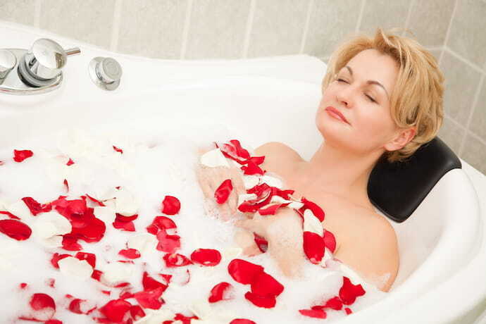 Mulher tomando banho em banheira com espuma e pétalas de rosa