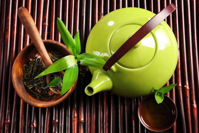 Bule de chá e alguns utensílios com ervas em cima de uma mesa de bambu 
