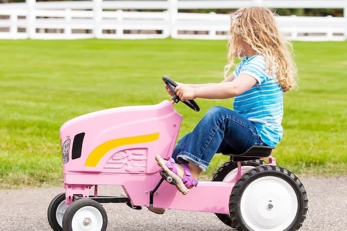 Menina andando em carrinho com pedal rosa.