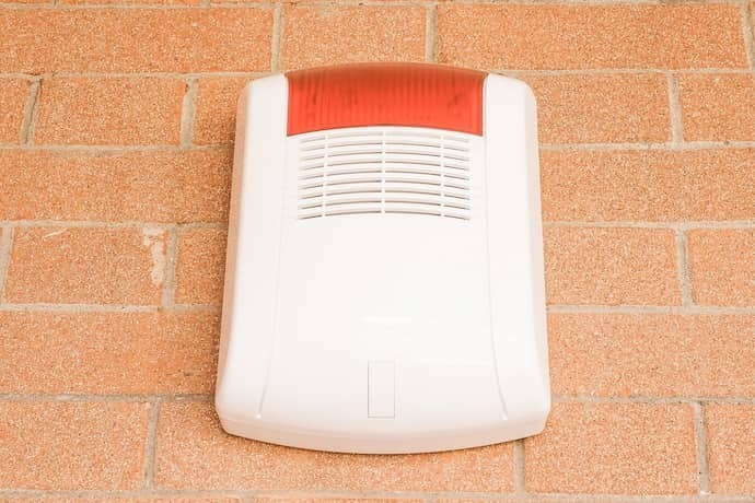 Alarme residencial branco e vermelho em parede de tijolos.