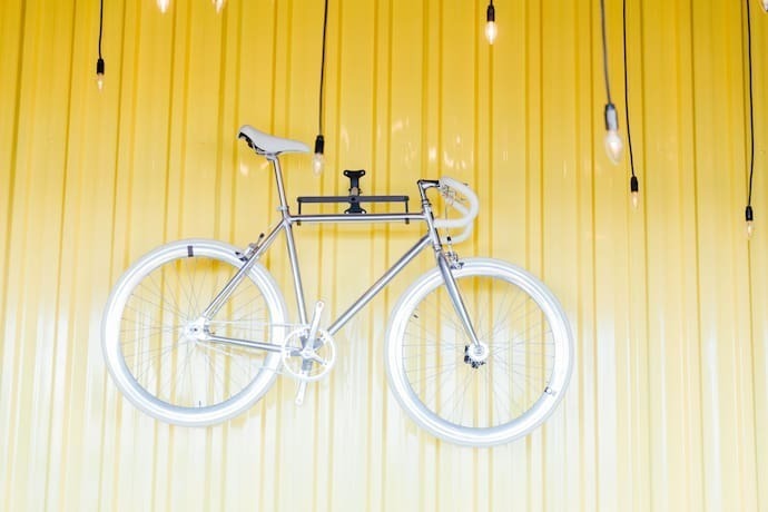 Bicicleta branca pendurada em parede amarela por suporte.