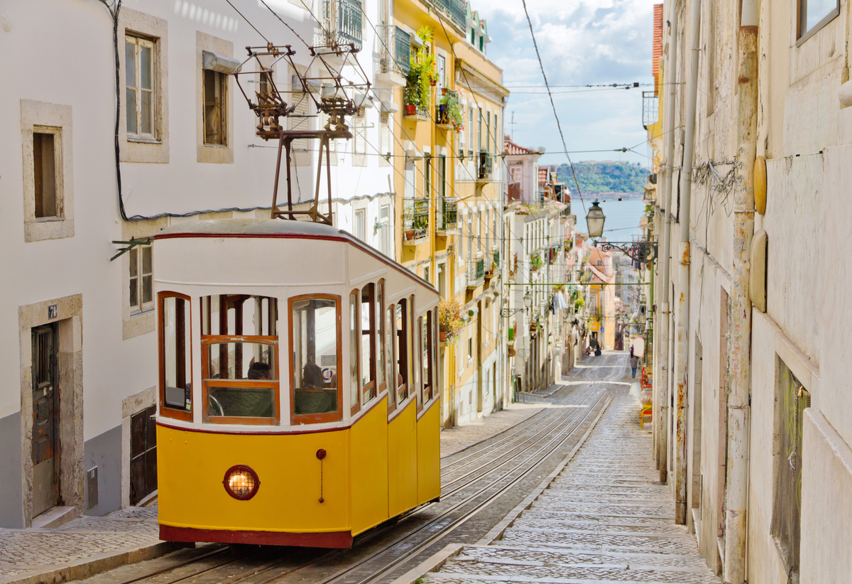 Bonde amarelo e branco numa rua estreita de Lisboa, Portugal