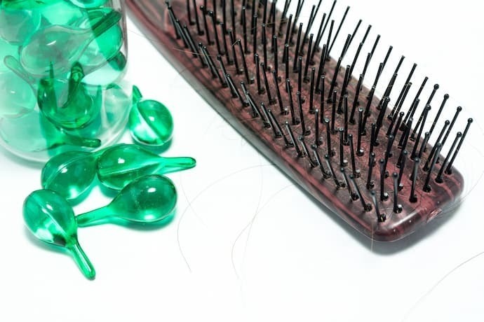 Vitaminas para queda de cabelo verde com escova ao lado.