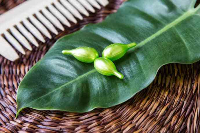 Vitaminas para queda de cabelo verdes em cima de uma folha ao lado de um pente.