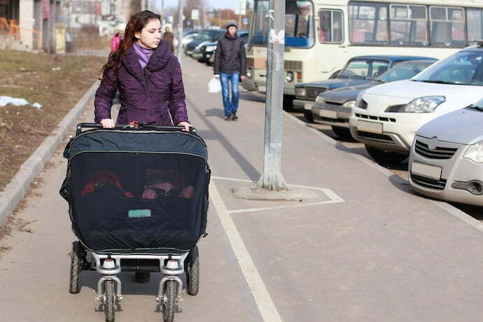Mãe empurrando carrinho de bebê para gêmeos