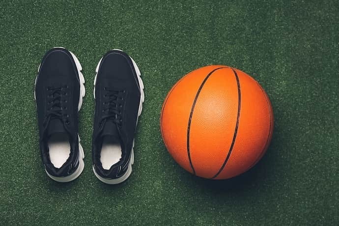 Tênis de basquete preto ao lado de bola de basquete em gramado sintético.