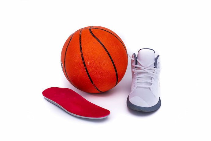 Tênis de basquete branco ao lado de bola de basquete e palmilha vermelha.