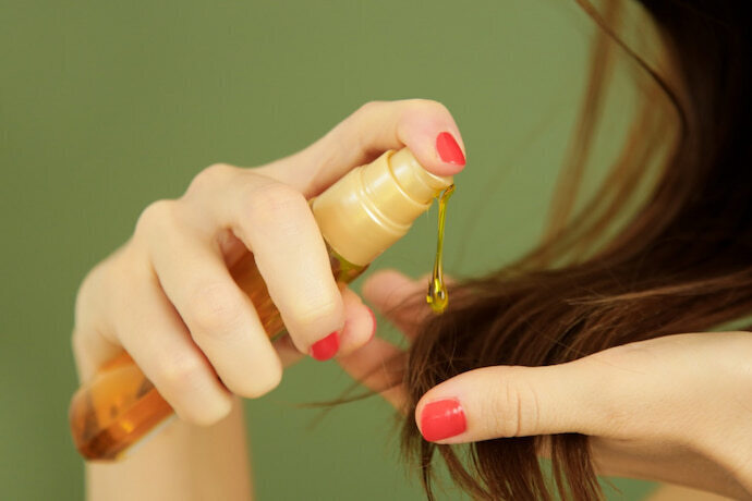 Mulher com recipiente de óleo para cabelo na mão passando o produto nos cabelos