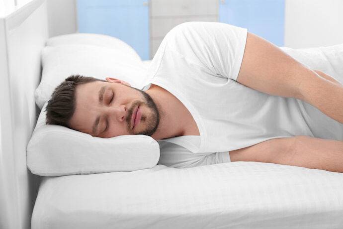 Homem dormindo de lado em travesseiro cervical.