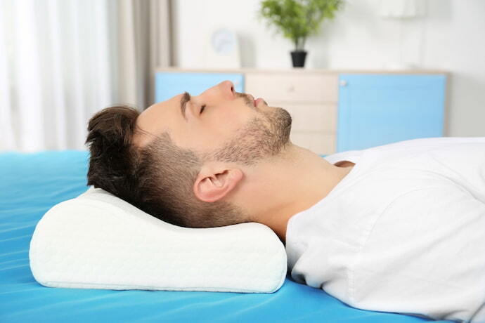 Homem dormindo para cima em travesseiro cervical.