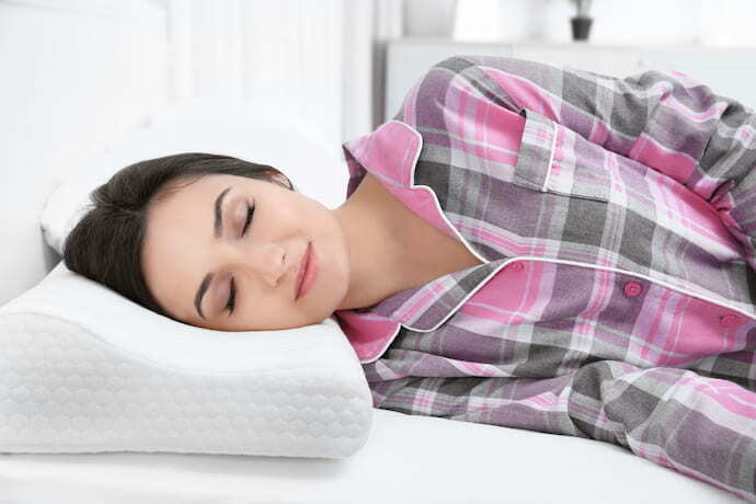 Mulher sorrindo dormindo em travesseiro cervical.
