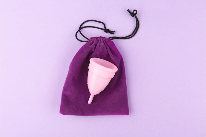 Coletor menstrual rosa em cima de saquinho roxo.