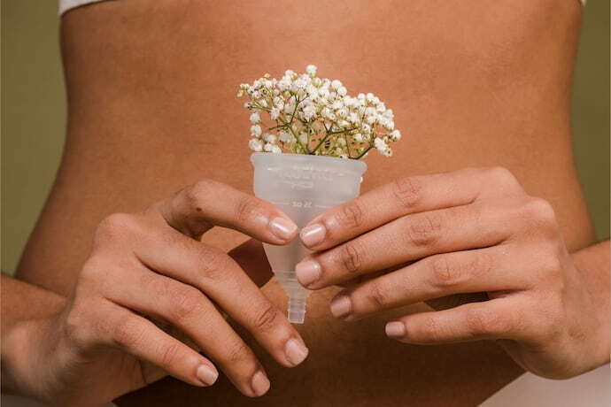 Mulher segurando coletor menstrual transparente com flores brancas dentro.
