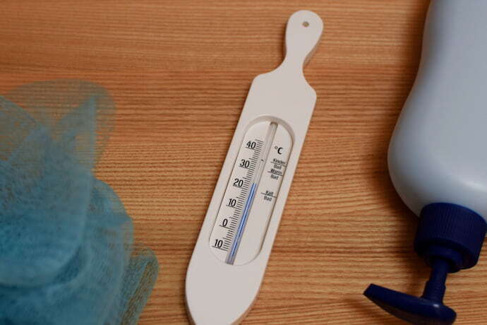 Termômetro de banheira branco com esponja e embalagem de produto de banho.