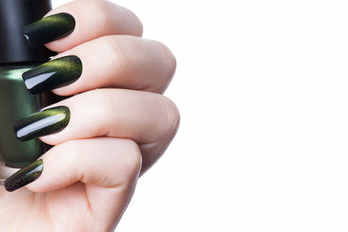Mulher de unhas pintadas e segurando esmalte verde