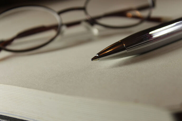 Caneta de ponta em cima de caderno e óculos.