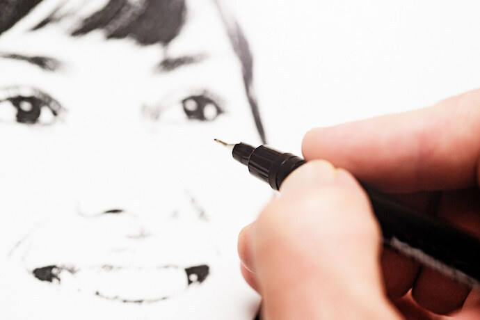 Pessoa desenhando com caneta preta de ponta fina. 