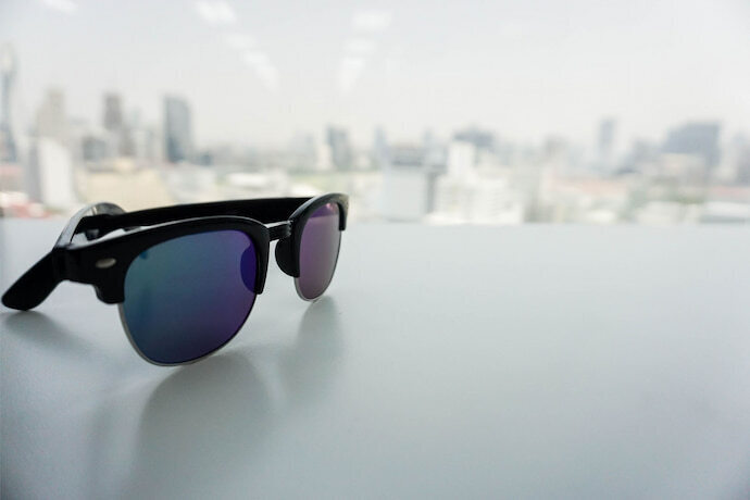 Óculos de sol masculino com vista de cidade ao fundo. 