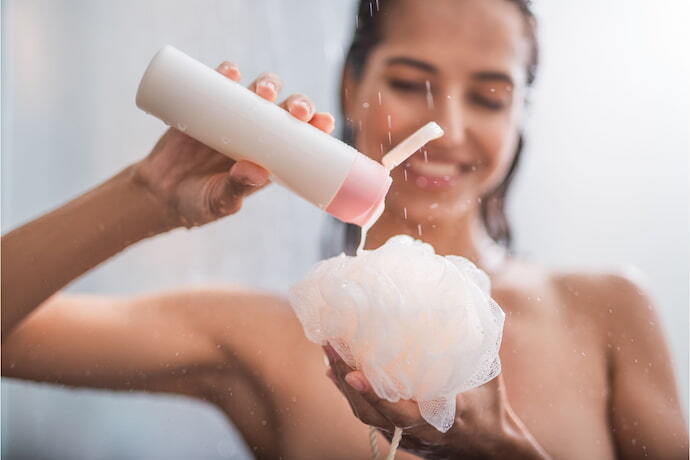 Mulher tomando banho colocando sabonete líquido em esponja de banho.