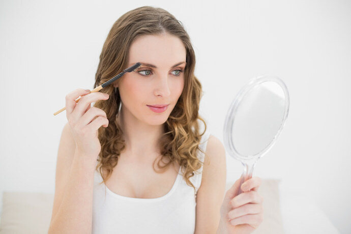 Mulher usando caneta para sobrancelha com um espelho