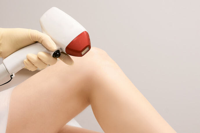 Pessoa segurando depilador a laser perto de uma perna feminina
