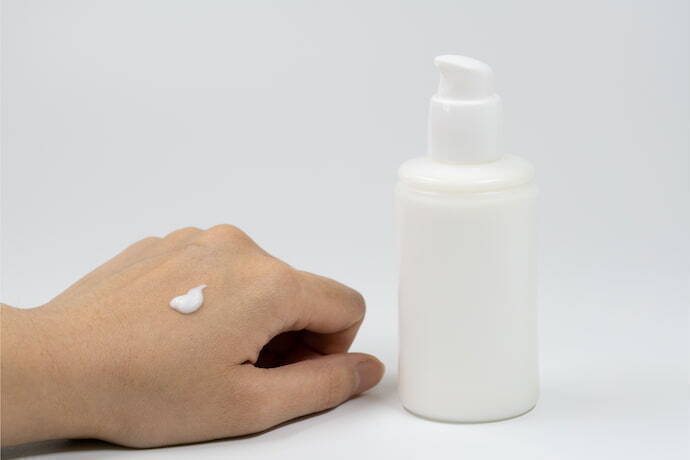 Pessoa com gota de hidratante na mão ao lado de embalagem 
